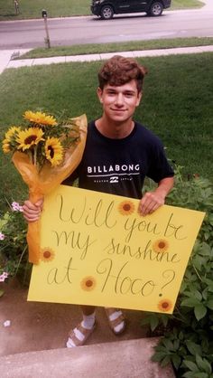 a young man holding a bouquet of sunflowers and a sign