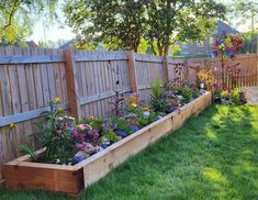 a wooden garden bed sitting on top of a lush green grass covered yard next to a fence