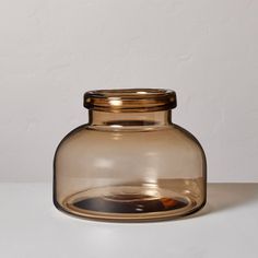 a glass jar with a gold lid on a white tableclothed surface in front of a plain wall