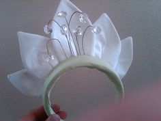 a person holding a white flower headband with crystal beads on it's side