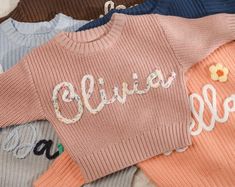 the sweaters are all different colors and have embroidered letters on them that spell out hello