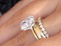 a woman's hand with two gold rings and an oval shaped diamond ring on it