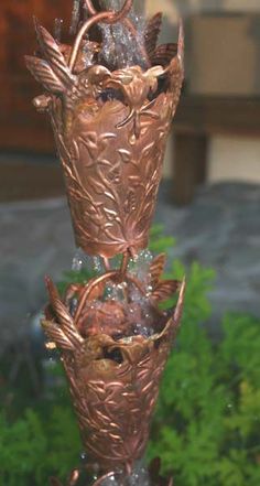 three metal vases sitting on top of each other in front of some plants and bushes