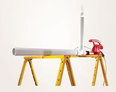 a red and white object is sitting on a yellow stand with two pipes attached to it