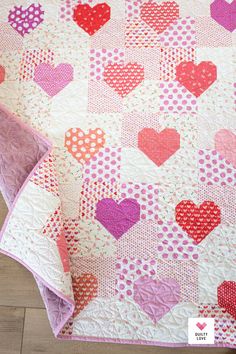 a pink and red heart quilt on top of a wooden floor next to a pillow