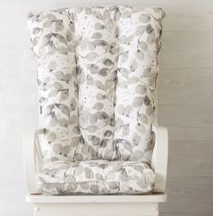 a white chair with a gray and white pillow on it's armrests