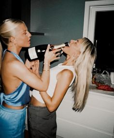 two women are drinking from bottles in the kitchen