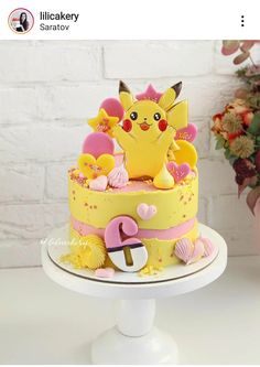 there is a yellow cake with pink and yellow decorations on the top it has a pikachu figurine sitting on top