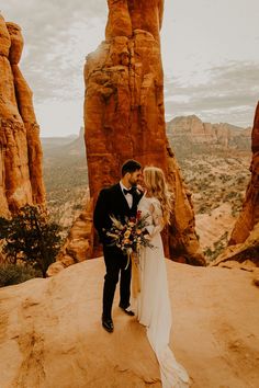 a bride and groom standing on top of a rock formation in front of the desert