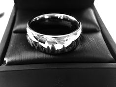 a silver ring with trees on it sitting in a black leather box, showing the inside