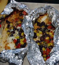 two pieces of pizza with black olives, corn and tomatoes in foil wrappers