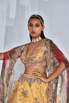 Editor's Note This is a pale yellow organza lehenga with a chiffon printed cape and an embroidered embellished leather belt. The lehenga has a flowy, ethereal look to it, while the chiffon cape adds an extra layer of sophistication to the outfit. The embroidered embellishments and leather belt add a touch of glamour and edge to the overall look. Fabric: Organza, chiffon Color: Yellow Components: Lehenga, cape, belt, blouse Occasion: Haldi mehndi Care: Dry Clean Only About the Designer Dolly J is Gold Organza Lehenga Hand Embellished, Eid Organza Dupatta With Cape Sleeves, Festive Sharara With Cape Sleeves In Organza, Festive Organza Sharara With Cape Sleeves, Festive Yellow Hand Embellished Set, Festive Hand Embellished Yellow Set, Bollywood Style Sharara With Cape Sleeves In Organza, Eid Organza Sharara With Cape Sleeves, Eid Yellow Embellished Choli