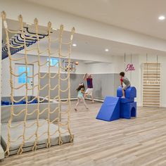 children playing in an indoor play area with ropes and climbing equipment on the floor, while adults watch