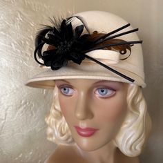 This Stunning 1960's Fashion Statement Consists Of A Rounded Crown Made Of Winter White Felt. There Is A Short Brim At The Front, And A Narrow Band Around The Crown Which Ends In A Bow At The Front. There Is A Beautiful Black Fabric "Flower" And Several Black "Stems" Attached At The Front, And Two Brown Curly Feathers. The Hat Wearing Requirement From Previous Decades Was Drastically Subsiding In The 1960s. Most Dressy Hats In The 1960s Were Worn By Women Who Embraced The Traditional Etiquette Rules Of Wearing Hats To Match The Occasion. Label: Michelle This Is An Authentic Piece Of Fashion History! This Hat Is In Wonderful Vintage Condition & Has Been Lovingly Preserved Among Over 1300 Etiquette Rules, Dressy Hats, 1960's Fashion, Feather Trim, 1960s Fashion, Fabric Flower, Trim Color, Winter White, Fashion History