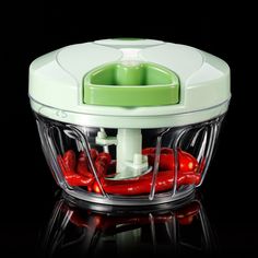 a green and white blender with red peppers in it's bottom basket on a black background