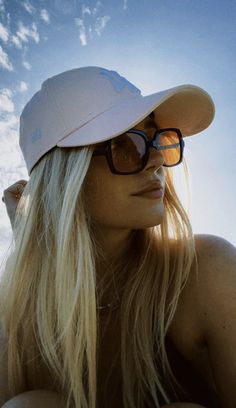 a woman wearing sunglasses and a hat is sitting on the beach with her head tilted to the side