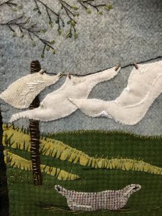 two white birds are flying in the sky above some trees and grass, while another bird is hanging from a wire