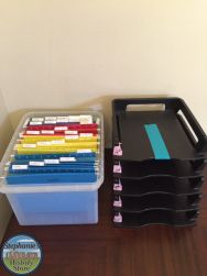 there is a plastic container with colored pencils in it next to a stack of file folders