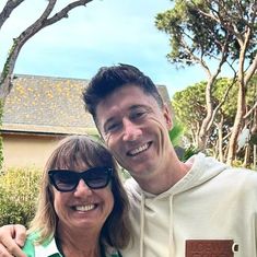 a man and woman standing next to each other in front of a house with trees