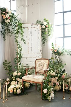 an arrangement of flowers and candles on the floor next to a chair in front of a window