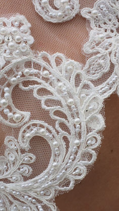 the back of a woman's wedding dress with white lace and pearls on it