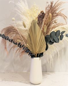 an arrangement of dried flowers in a white vase