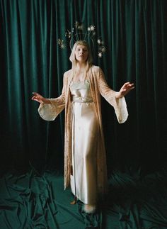 a woman in a white dress is standing with her hands out and wearing a crown