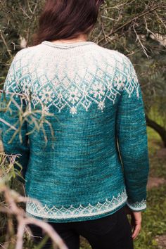 a woman standing in the woods wearing a green and white sweater