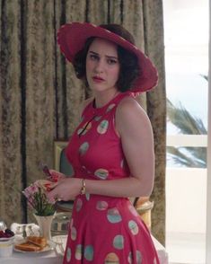 a woman in a pink dress and hat standing next to a table