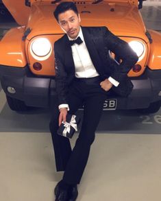 a man in a tuxedo sitting on the ground next to an orange jeep