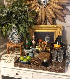 a white table topped with bottles and glasses next to a potted plant on top of a dresser