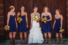 a group of women standing next to each other in front of a wooden fence holding bouquets