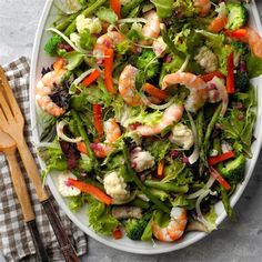 a salad with shrimp and broccoli on a plate next to utensils