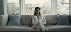 a woman sitting on top of a couch next to two windows