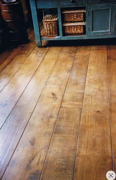 an old wooden floor in a kitchen with blue cabinets and baskets on the top shelf