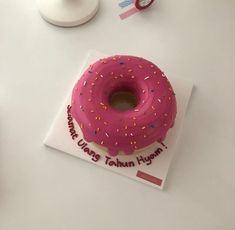 a pink frosted doughnut with sprinkles on it sitting on top of a card