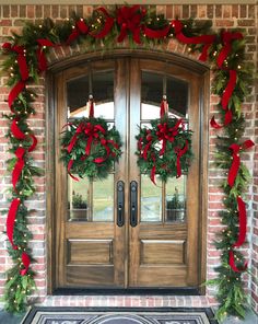 two christmas wreaths on the front door of a brick house with red bows and greenery