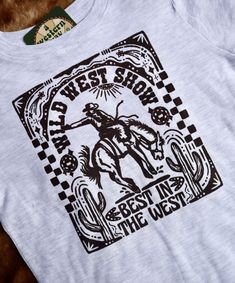 Are you ready for the show? Our Wild West Show Tee is best in the west and ready to be your new favorite tee. Available in baby, toddler, and adult sizes, you can match your little one just in time for rodeo season. Please note:-Sizes 0-6 Months - 7 come on a short sleeve t-shirt-Adult sizes come on a short sleeve t-shirt-Since the baby + toddler and adult tees are different brands, the colors will slightly vary. ⋆ True to size⋆ Baby + Toddler sizes - 99% Cotton/1% Cotton Ash Rabbit Skins Tee⋆ A White Crew Neck Tops For Western-themed Events, White Graphic Tee For Western-themed Events, Crew Neck Top With Graphic Print For Western-themed Events, Graphic Print Crew Neck Tops For Western-themed Events, Graphic Tee With Screen Print For Western-themed Events, Graphic Tee T-shirt For Western-themed Events, Short Sleeve Graphic Print T-shirt For Western-themed Events, Graphic Print T-shirt For Western-themed Events, White Graphic Print T-shirt For Western-themed Events