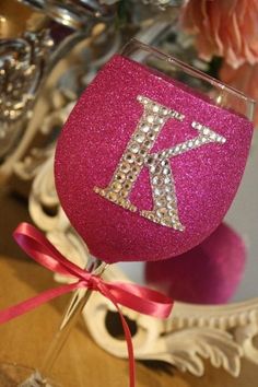 a pink wine glass with the letter k on it sitting in front of a mirror