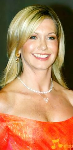 a woman in an orange dress smiling at the camera and wearing a diamond necklace on her neck