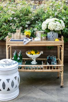 a wicker bar cart with lemons and bottles on it in front of some bushes