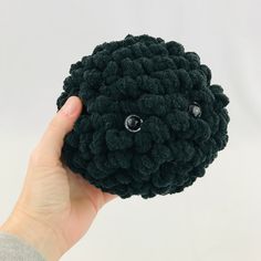 a hand holding a black crocheted object with eyes on it's face