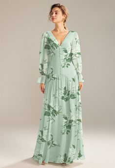 a woman in a long green dress with flowers on the front and sleeves, standing against a