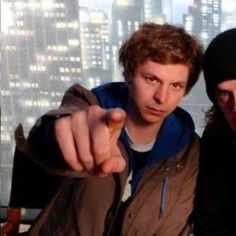 two young men pointing at the camera in front of a cityscape with skyscrapers