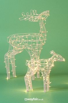 two lighted reindeers standing next to each other on a green background with white lights