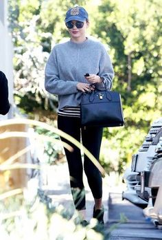 a woman in grey sweater and black leggings walking down street with handbag