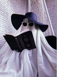 a person dressed up as a ghost reading a book while wearing sunglasses and a hat