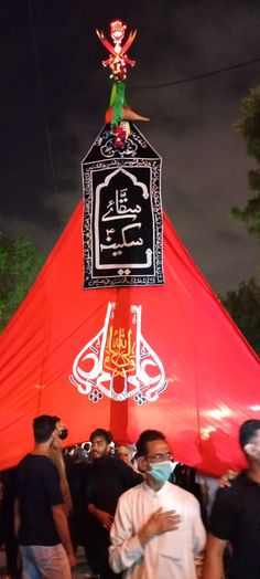 a group of people standing in front of a red tent with an arabic writing on it