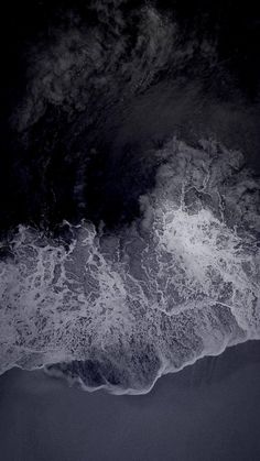 an aerial view of the ocean with waves coming in from the shore and dark clouds overhead