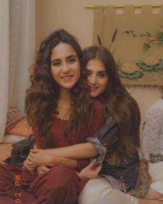 two young women sitting next to each other on top of a bed in a room